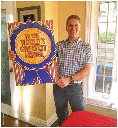 Photo of Todd Warren holding a large board that reads "To the world's greatest father".