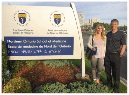 Photo of the author with her father when she started medical school in front of sign for Northern Ontario School of Medicine.