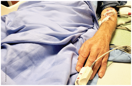 Close-up photo of the arm of an elderly man lying in a hospital bed with an IV.